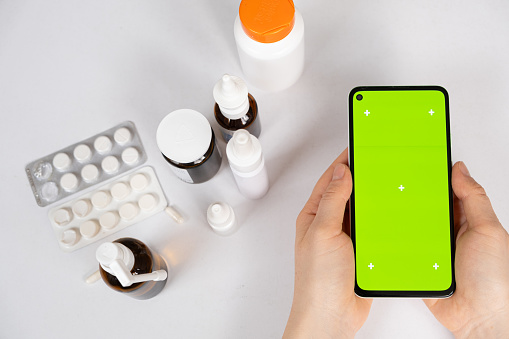Green screen chroma key smartphone in the hands of patient or doctor and a lot of medicines. Medicine, instructions for use.