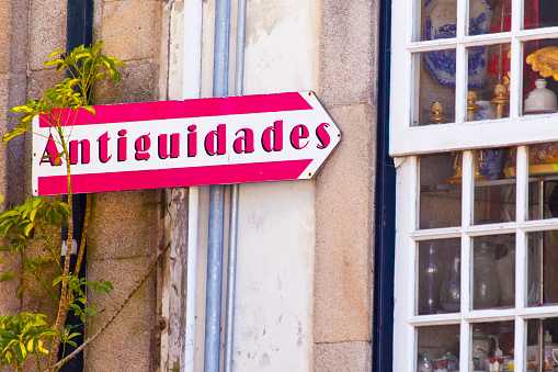Close-up view of Antiquities store sign on building facade, traditional stone house, window in the foreground. Valença do Minho, Portugal.