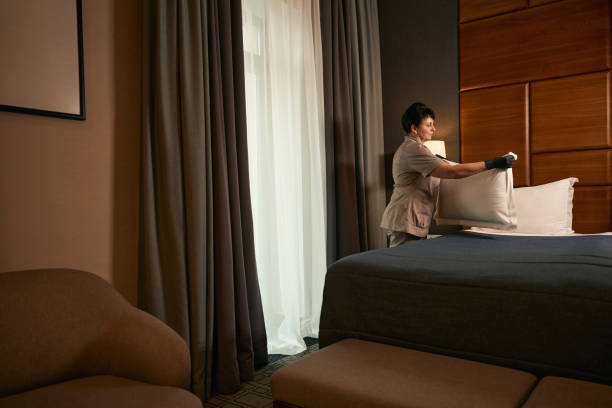 istock Uniformed maid involved in bed-making procedure in hotel room 1882030373