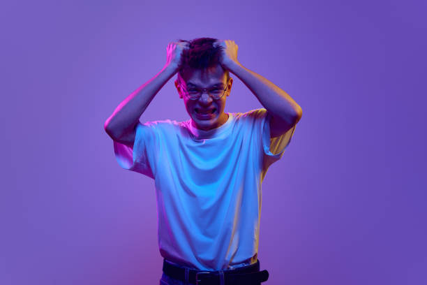 istock Young guy in casual clothes holding hands on head, expressing anger, irritation and stress against purple background in neon light 1882082192