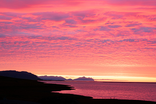Silhouette of a rocky coastline in the red light of a dramatic dawn. Dark dawn photo with red sky. Iceland