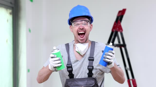 Portrait of a positively emotional joyful construction worker painter splashes from spray can