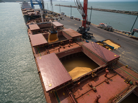 Imbituba, Brazil – September 10, 2020: aerial view of two cranes loading soybeans onto a cargo ship, with the ship's holds full, ready for export