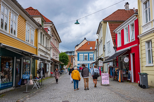 Bergen, Norway, June 22, 2023: A group of people walks on a  vacant cobblestone street in the city center of Bergen after a rainstorm. The Hollendergaten cobblestoned pedestrian shopping street.
