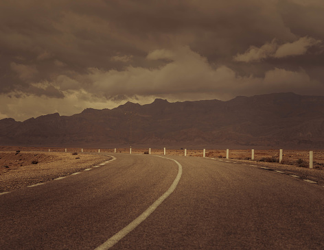 The empty asphalt road through the desert during the cloudy sandy day in Northern Africa (Tunisia).