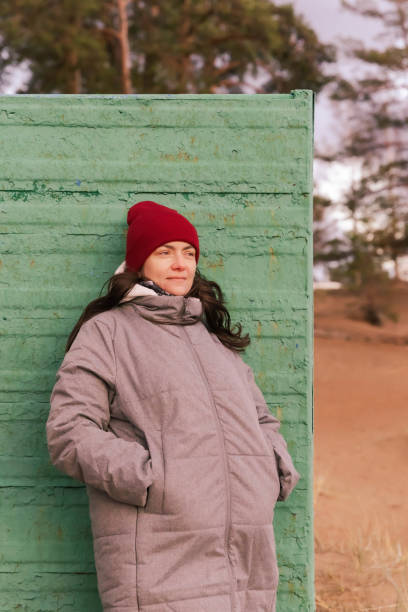 istock Woman in Red Hat Walking Along Autumn Beach Posing by Old Changing Booth 1882198778