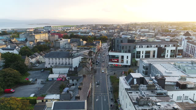Drone shot moving up from overhead bustling city street to sunset skyline over Galway, Ireland.