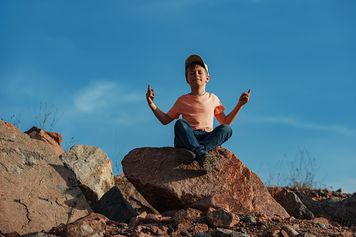 Boy sitting in meditation pose on rock in the mountains