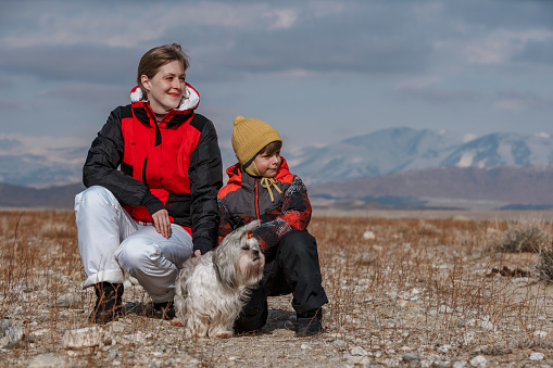 Mother, son and shih tzu dog looking away on winter mountains background
