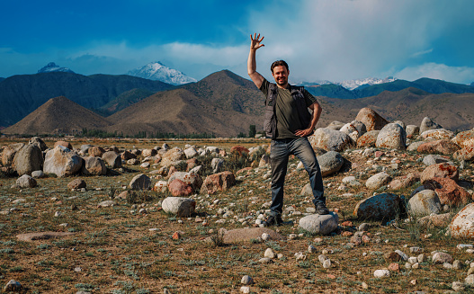 Young smiling man stands on mountain and waving his hand