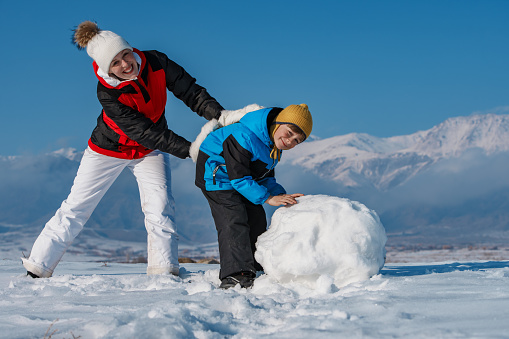 Happy mom and son making a snowman in the mountains