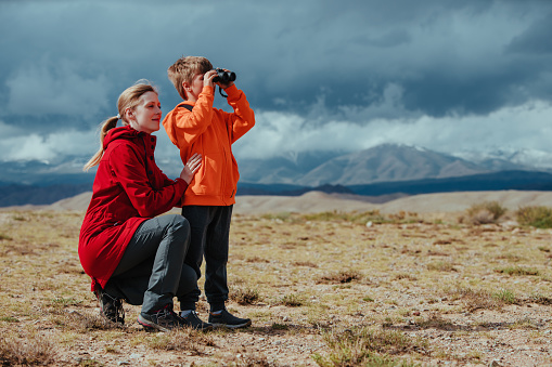 Boy tourist with binoculars and his mother in mountains