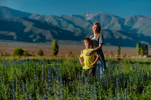 Happy young woman with her son posing in a blooming meadow on mountains background