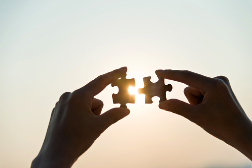 Woman hand putting puzzle pieces together in sunset.