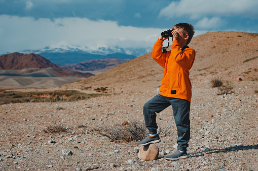 Boy tourist looking in binoculars in mountains