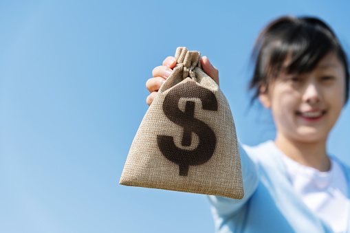 Woman holding money bag under blue sky.