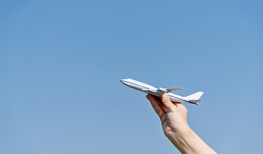 Woman hand holding model airplane under blue sky.
