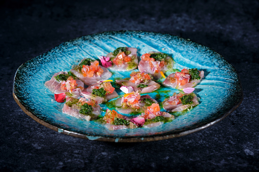 High angle of delicious bites of fish with sauce and flowery vegetable in blue sauce on plate placed over dark marble table background