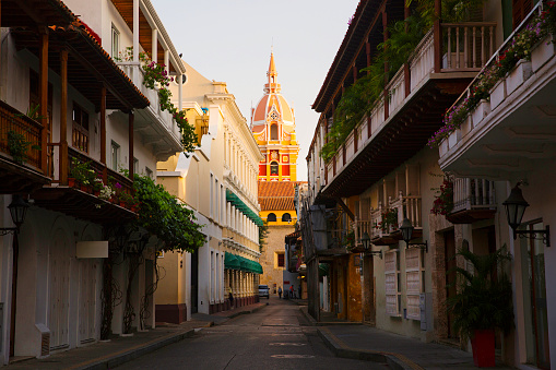A charming street with the spire of a church at the end, in the old central part of Cartagena - Cartagena is a port city on Colombia’s Caribbean coast, a historic city of superbly preserved beauty lying within 13km of centuries-old stone walls. And a very popular tourist destination