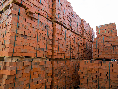 Pallets with red bricks are stored in an open area.