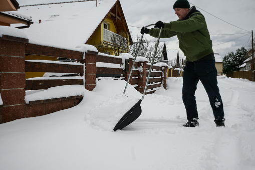 guy in jacket, hat and gloves shovels snow in front of house after blizzard - close up view.