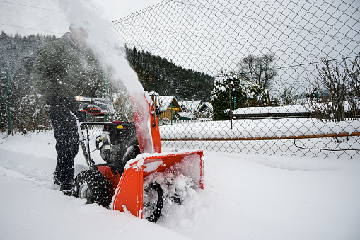 man shovels snow with a red snowblower, snow splashes to the side - close-up view.