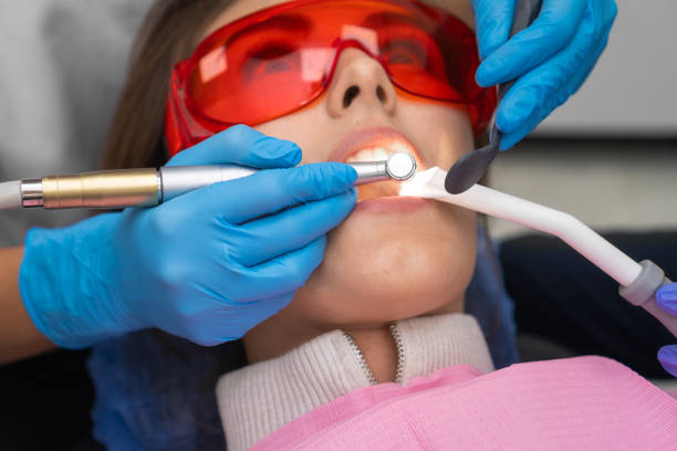 le dentiste en close-up utilise une perceuse et un miroir dentaire pour traiter les dents d’une jeune patiente portant des lunettes de protection. concept d’hygiène dentaire et de santé. - dental hygiene dental equipment dental drill practicing photos et images de collection