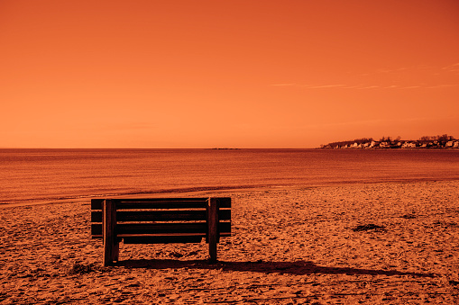 Dramatic fiery monochromatic deserted beach scene with an empty bench and footprints