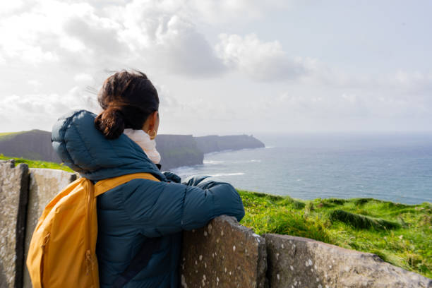 istock Woman on her back with backpack contemplating a beautiful seascape next to the Cliffs of Moher in Ireland on a bright day 1882429337
