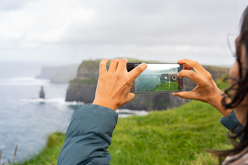 Close-up of hands taking a phothograph with cell phone from the top of the Cliffs of Moher in Ireland