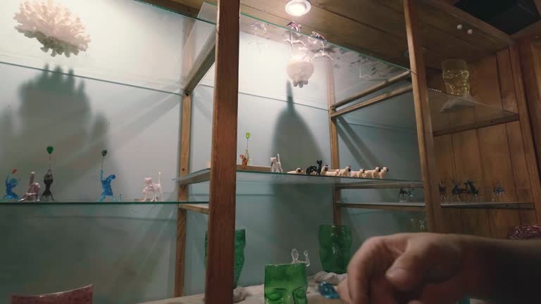 a young man places his new designs on the shelves of his workshop showcase