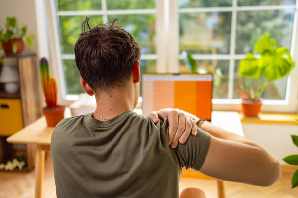 istock Unrecognizable young man experiencing a pain in shoulder, while e-learning at home 1882552552