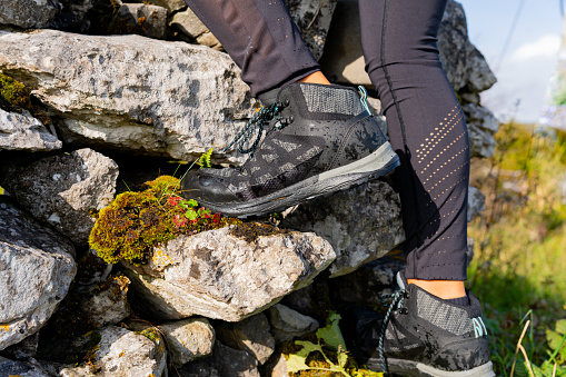 Close up of legs in hiking boots of a woman climbing a small stone wall in an Irish landscape