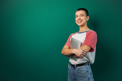 Studio portrait of a beautiful, young, smiling woman with short hairstyle, holding a digital tablet.