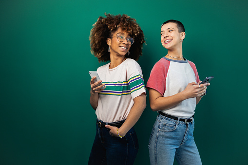 Studio portrait of the two best female friends of different ethnicity using smartphones and having fun together.