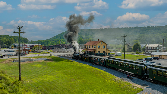 Rockhill Furnace, United States – August 05, 2023: An Aerial View of a Narrow Gauge Steam Passenger Train, Arriving into the Station, Blowing Smoke, on a Sunny Summer Day