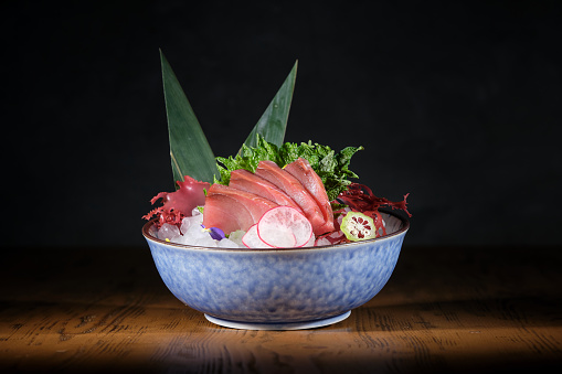 Bowl with yummy sashimi with fresh fish fillet and radish and lime placed on ice decorated with banana leaves