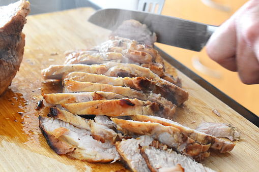 Roasted pork slices on bamboo chopping board. Christmas meal cooking preparation.