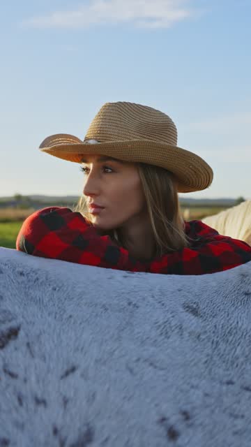 SLO MO Thoughtful Young Female Rancher in Cowboy Hat Leaning on White Horse on Meadow on Sunny Day