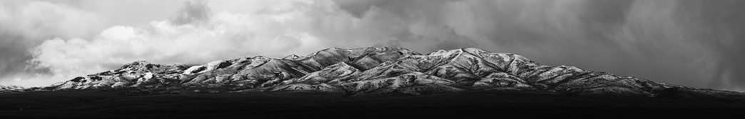 A dramatic black and white photograph depicting a majestic mountain beneath a tumultuous sky
