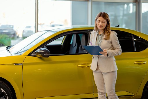 Beautiful Young Woman Working as Car Seller. She is Using Clipboard and Checking Car Before Customer or Buyer