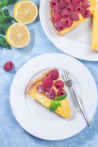 Piece of delicious lemon tart with fresh raspberry, on plate, vertical, top view, closeup