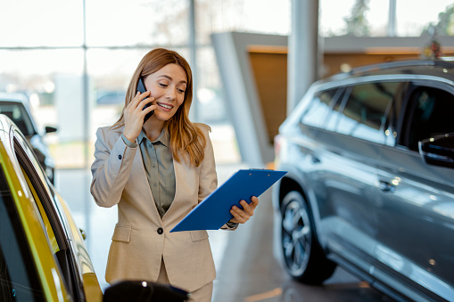 Young Saleswoman Talking on Smartphone in a Car Showroom