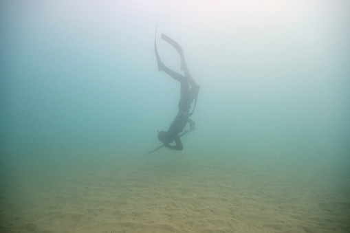 Full body side view of anonymous underwater fisherman in wetsuit and flippers with harpoon diving in deep seawater