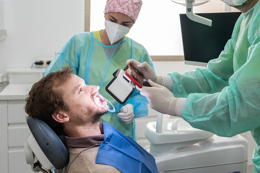A dentist taking pictures of a patient's mouth with an imaging device attached to a mobile phone.