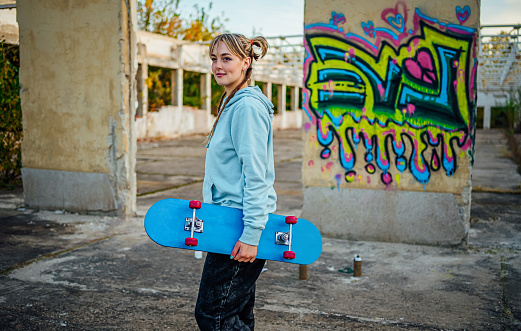 Cheerful young woman with her skateboard standing in front of a wall with colorful graffiti