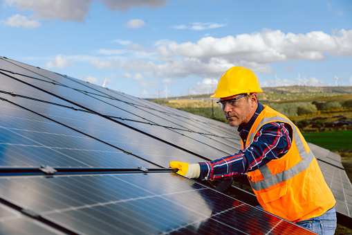 Embark on the journey of renewable energy with this dynamic stock photo, featuring a worker installing a replacement and moving a solar panel at a solar farm. Concurrently, engineers are checking the operation of the system, symbolizing the dedication to alternative energy solutions and the conservation of the world's energy. The photovoltaic module idea further emphasizes innovation for clean energy production. Perfect for conveying the collective effort towards a sustainable future, this photo is ideal for energy-related promotions, environmental publications, and social media content advocating for the global adoption of clean energy. Worker, Installing replacement, Moving, Solar panel, Solar farm, Engineers, Checking operation, Alternative energy, World's energy conservation, Photovoltaic module, Clean energy production, Dedication, Innovation, Stock photo, iStock, Energy-related promotions, Environmental publications, Social media, Sustainable future.