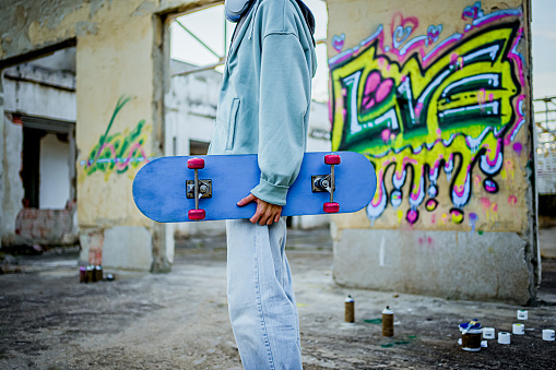 Young man with a skateboard standing in front of a wall with colorful graffiti