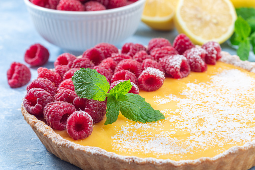 Homemade lemon tart, garnished with fresh raspberry, icing sugar and mint, horizontal closeup