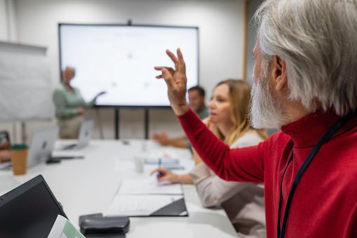 Senior adult worker raising hand while attending financial report presentation in office meeting room